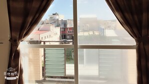 A window with brown curtains, a view of buildings, and a green gate. - Coffee Bear (Hengchun)