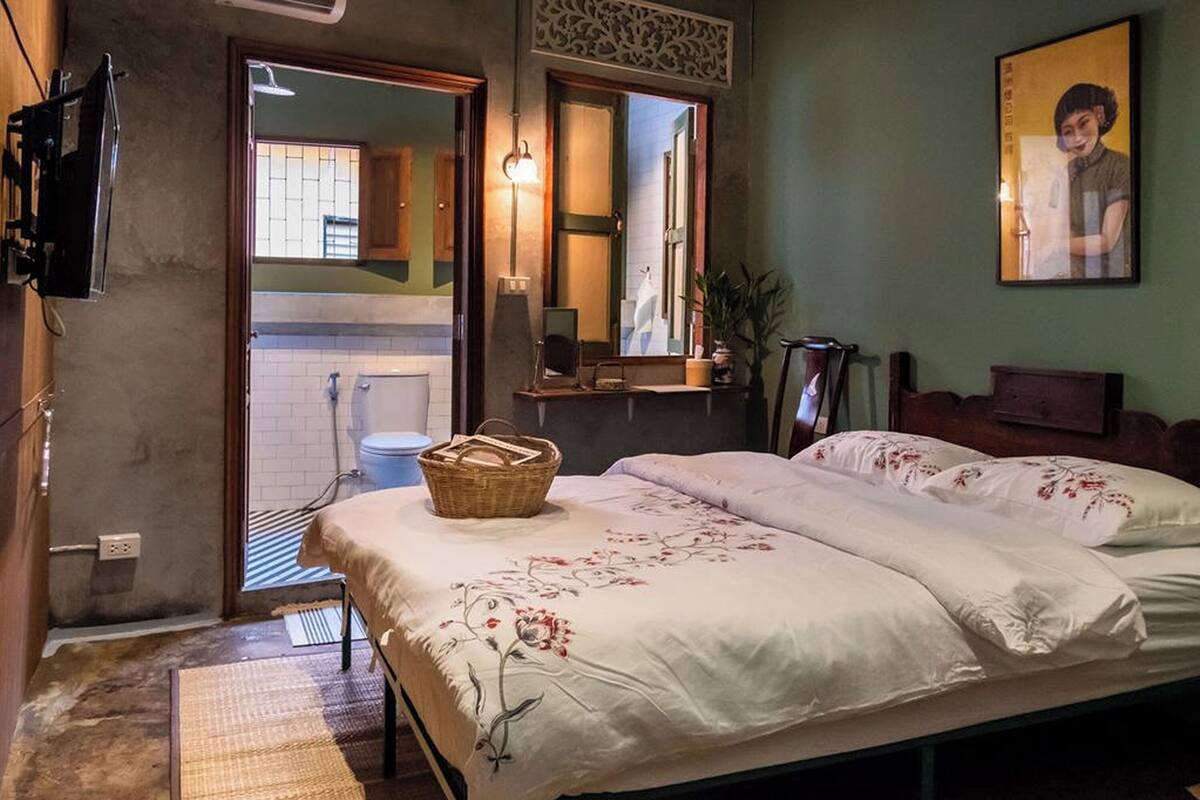 A bedroom with a bed, a bedside table, a mirror, a wall-mounted TV, and a bathroom visible through an open door.