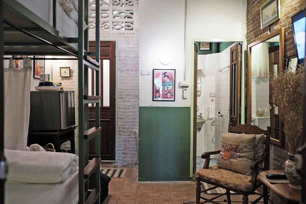 A narrow hallway with a bed, a chair, and a bathroom with a sink and mirror.