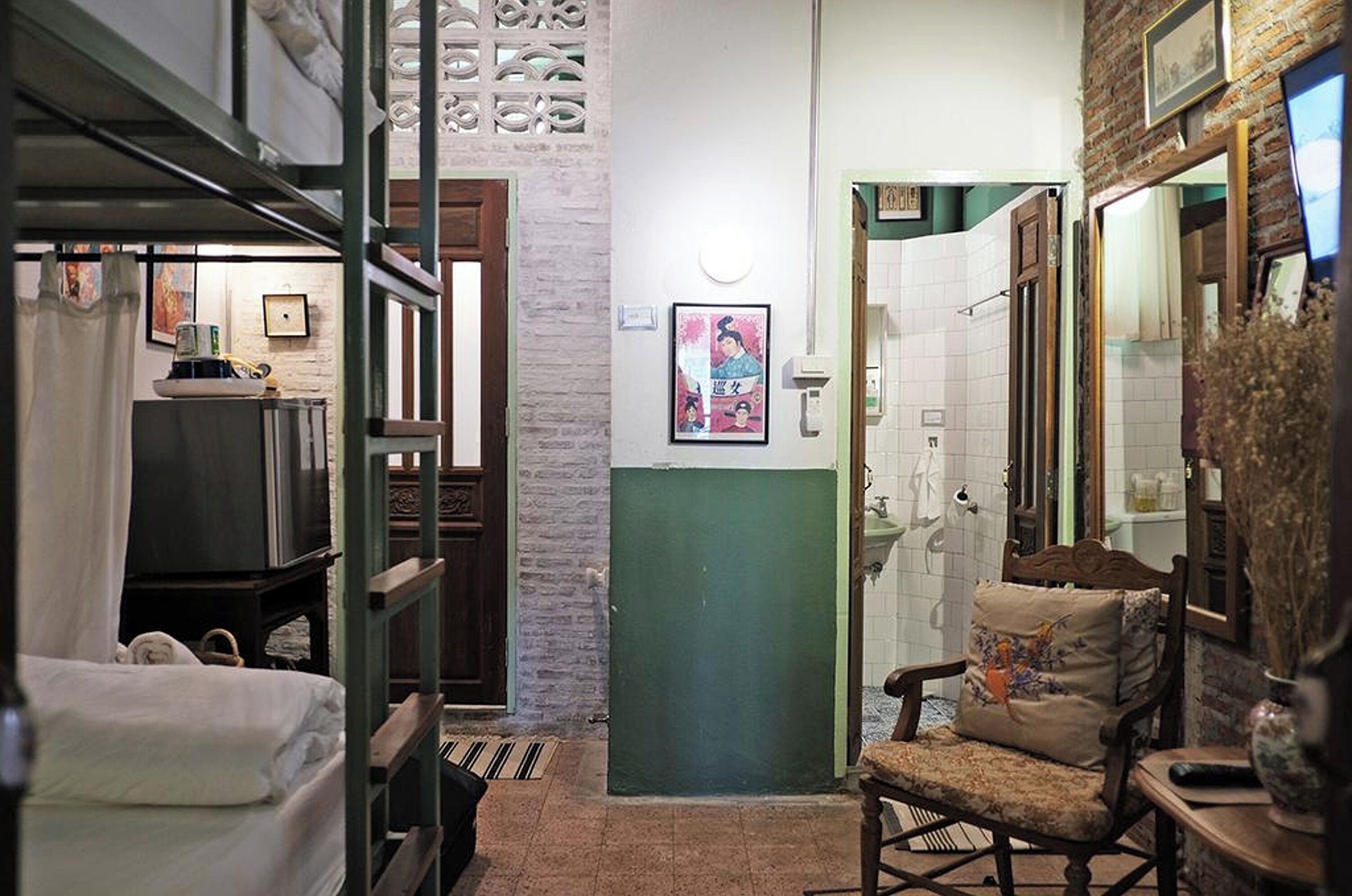 A narrow hallway with a bed, a chair, and a bathroom with a sink and mirror.