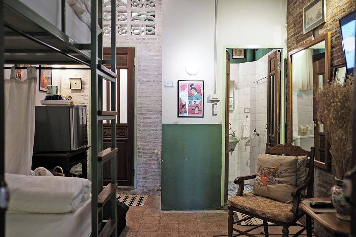 A narrow hallway with a bed, a chair, and a bathroom with a sink and mirror.