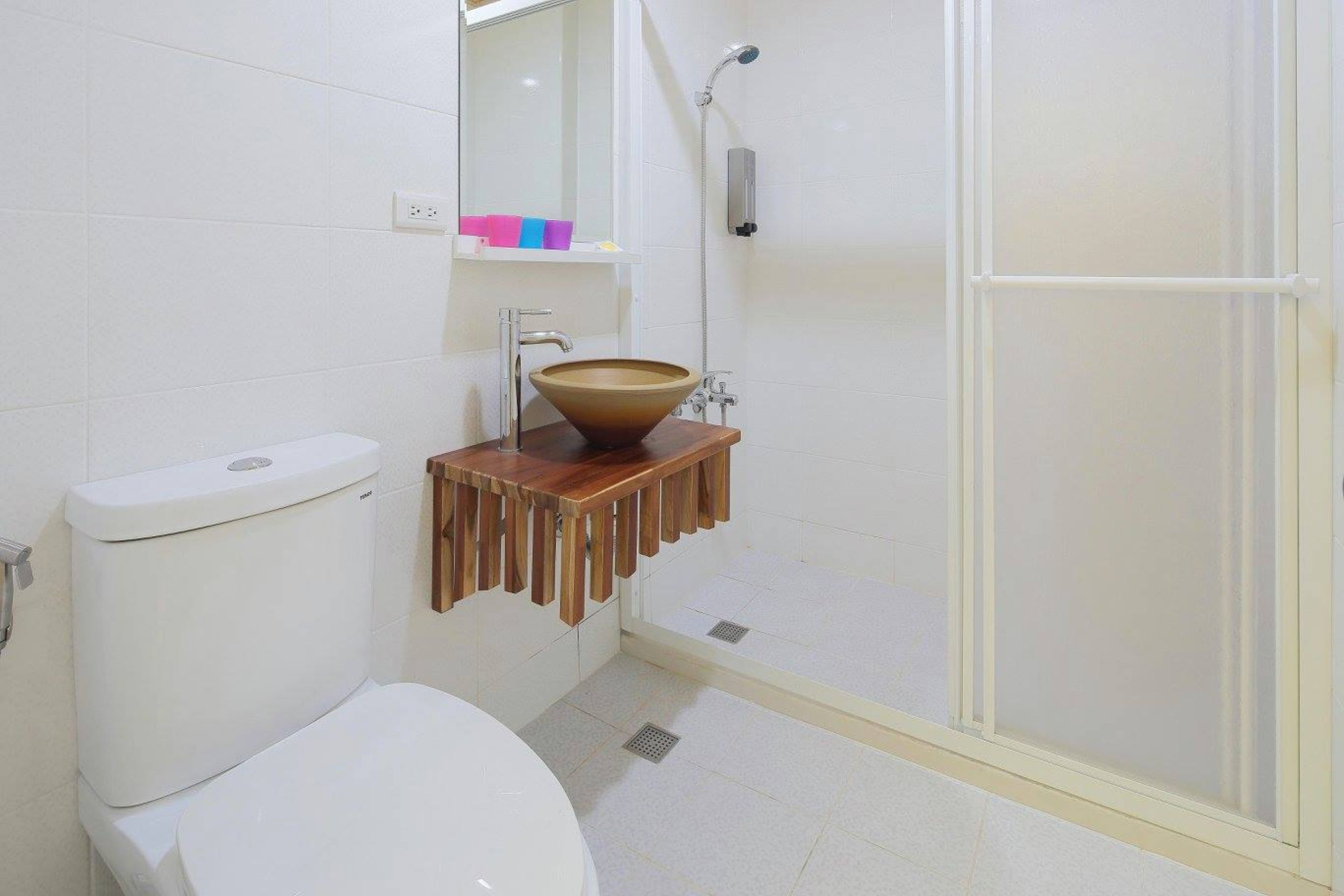 A bathroom with a white toilet, a wooden sink with a bowl, a mirror, and a shower area.