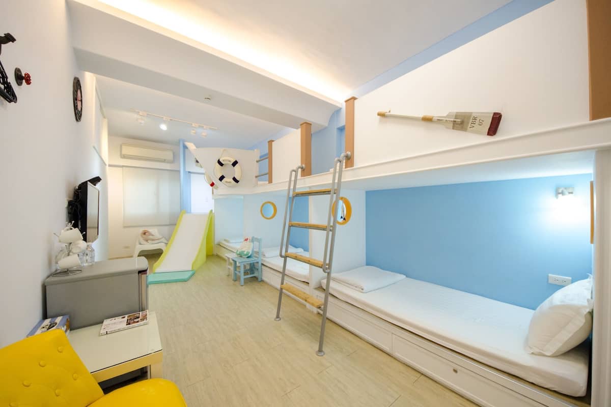 Quarto de criança com beliches, uma escada, uma escrivaninha e uma cadeira pequena.