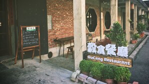 Ein GuCang Restaurant mit Backsteinwand und Holzstühlen vor der Fassade.