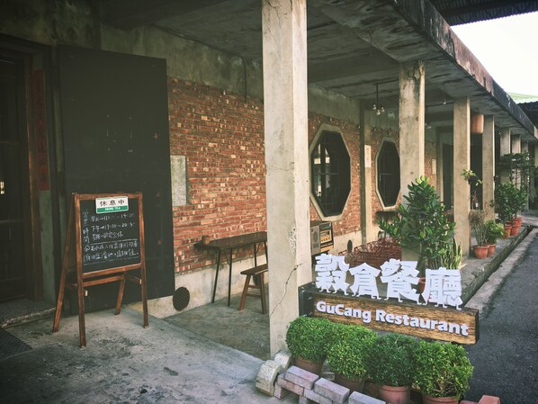 A GuCang Restaurant with a brick wall and wooden chairs outside.