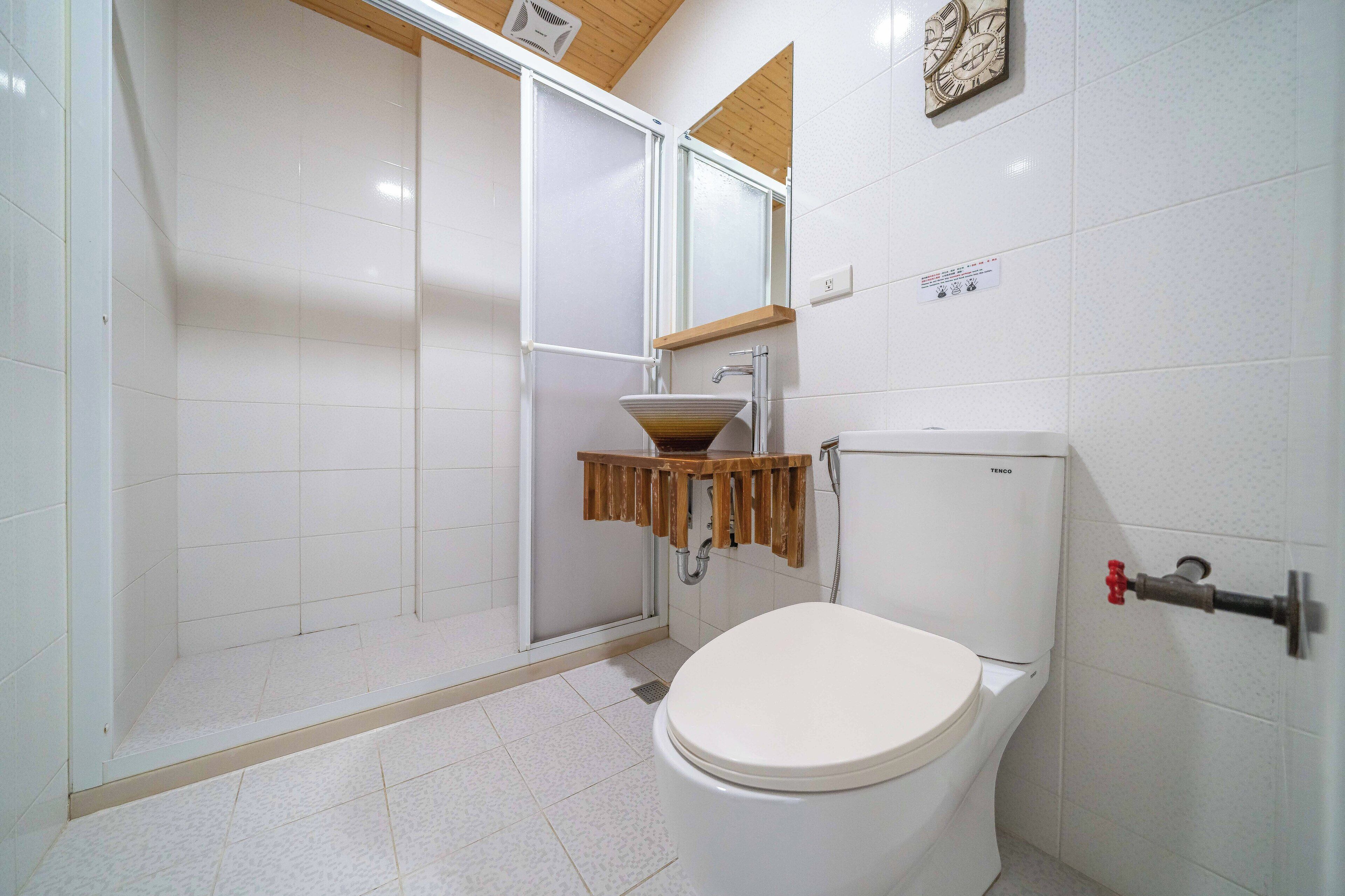 A bathroom with a toilet, a sink with a wooden countertop, and a shower area.