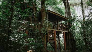 A wooden treehouse with a metal roof, surrounded by dense forest.