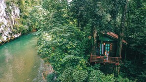 A wooden cabin with a balcony overlooking a river, surrounded by dense forest. - Our Jungle House (Phanom)