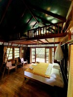 Una cabaña de madera con habitación en el altillo, balcón y comedor con mesa y sillas.