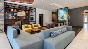 Een moderne woonkamer met een modulaire bank, gele fauteuils, een salontafel en een groot abstract schilderij.