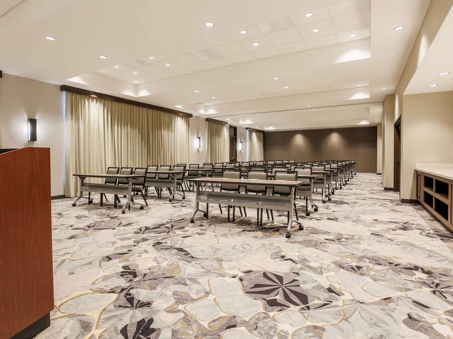 Un salón de conferencias con filas de mesas y sillas, un atril y una alfombra estampada.