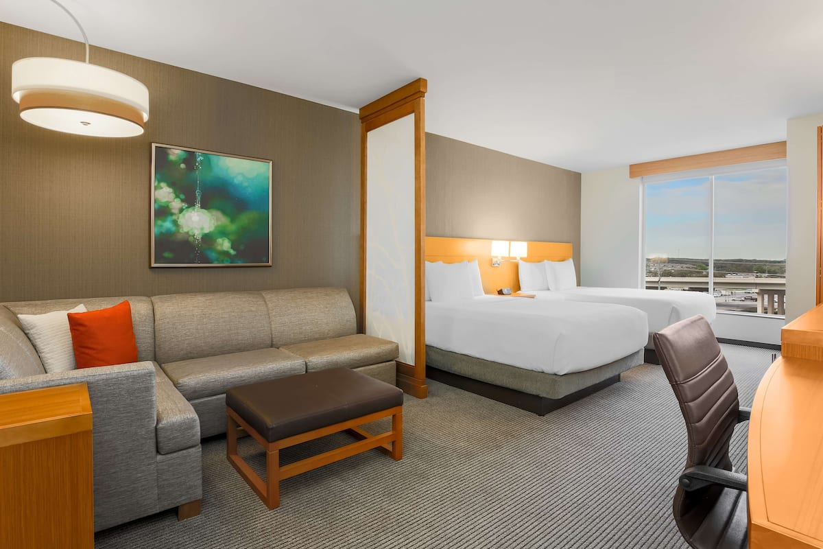 A hotel room with a large bed, a sofa, a desk, and a view of the city through the window.