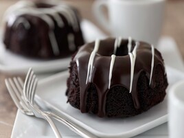 Um bolo bundt de chocolate com cobertura branca sobre um prato branco.