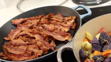 A kitchen with a frying pan containing bacon and a pot with vegetables.