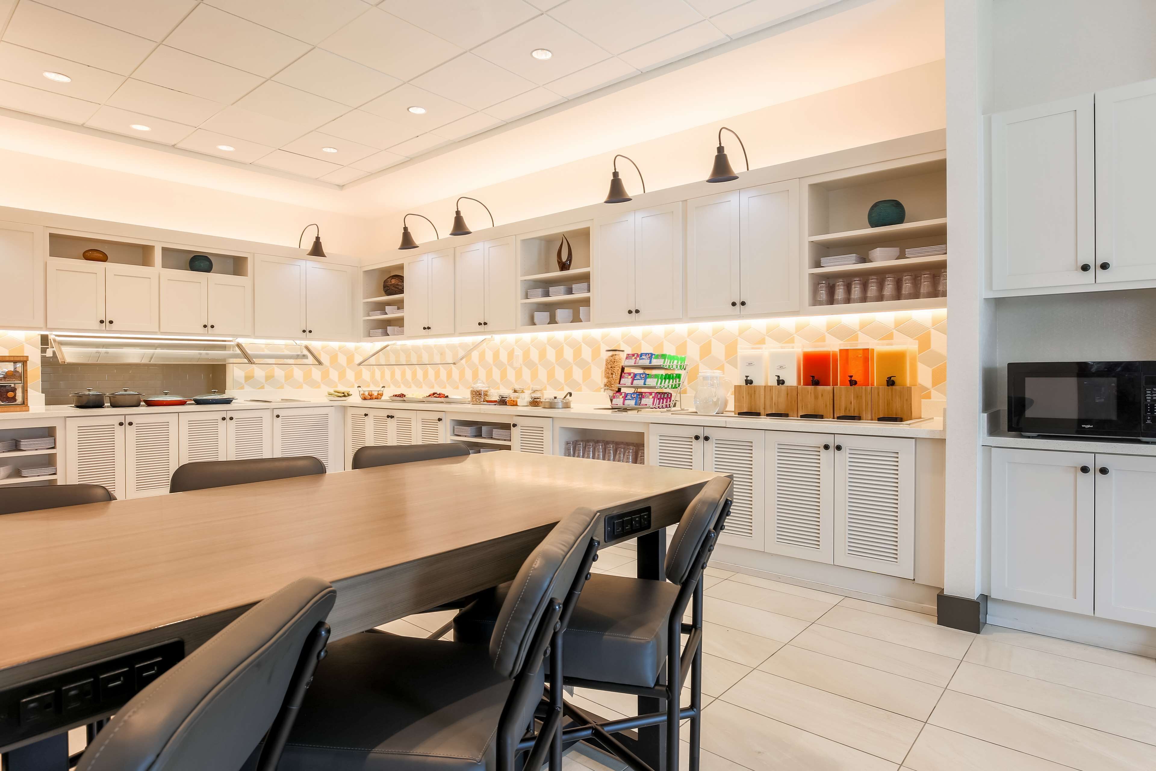 Una cocina moderna con armarios blancos, una mesa de comedor de madera y sillas negras.