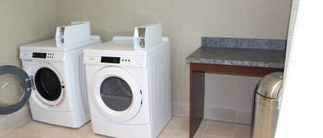 A laundry area with two white washing machines, a small table, and a trash can.