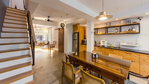 A modern kitchen with wooden cabinets, a dining table, and chairs. There is a staircase on the left and a door leading to another room. - Tree House (Tainan)