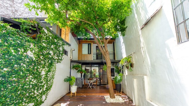 A narrow courtyard with a wooden deck, a dining area, and a tree. - Tree House (Tainan)