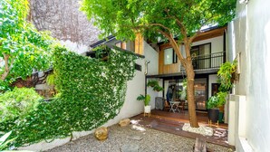 A modern outdoor patio area with a wooden deck, stone steps, and lush greenery. - Tree House (Tainan)