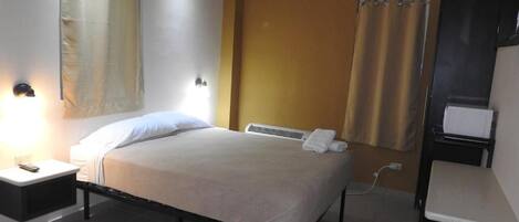 Una habitación de hotel con cama, mesita de noche y zona de ducha.