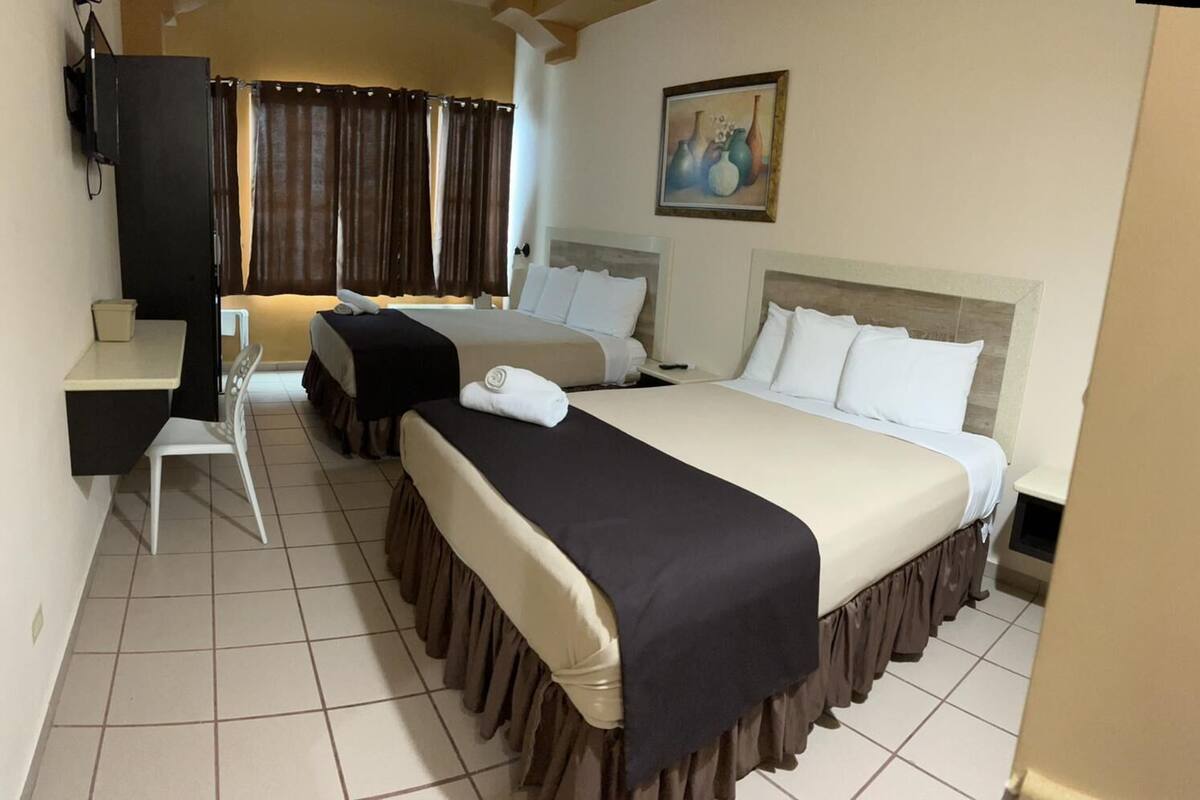 A hotel room with two beds, a desk, and a television.