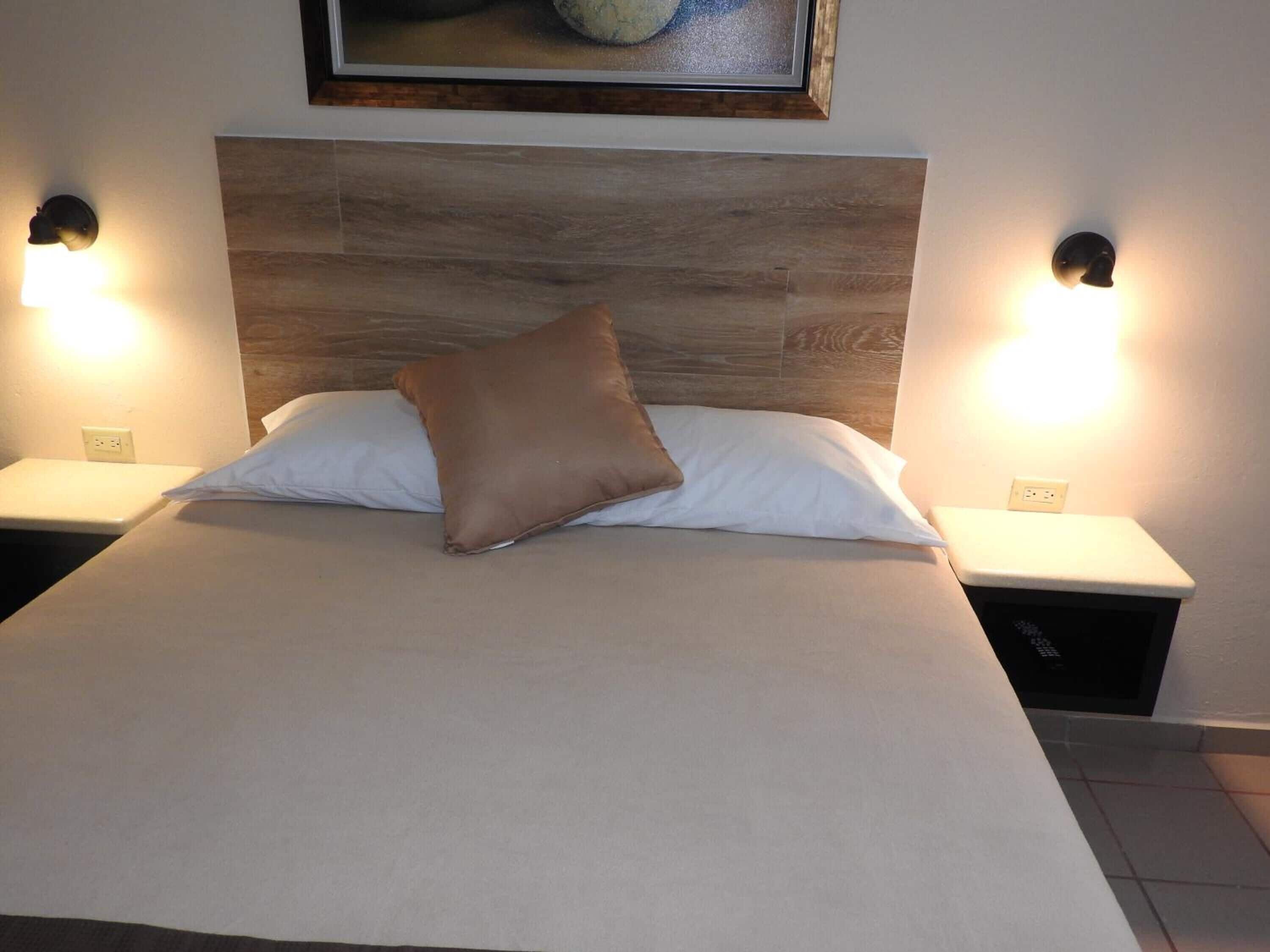 A neatly made bed with a pillow, two bedside lamps, and a nightstand with a power outlet.