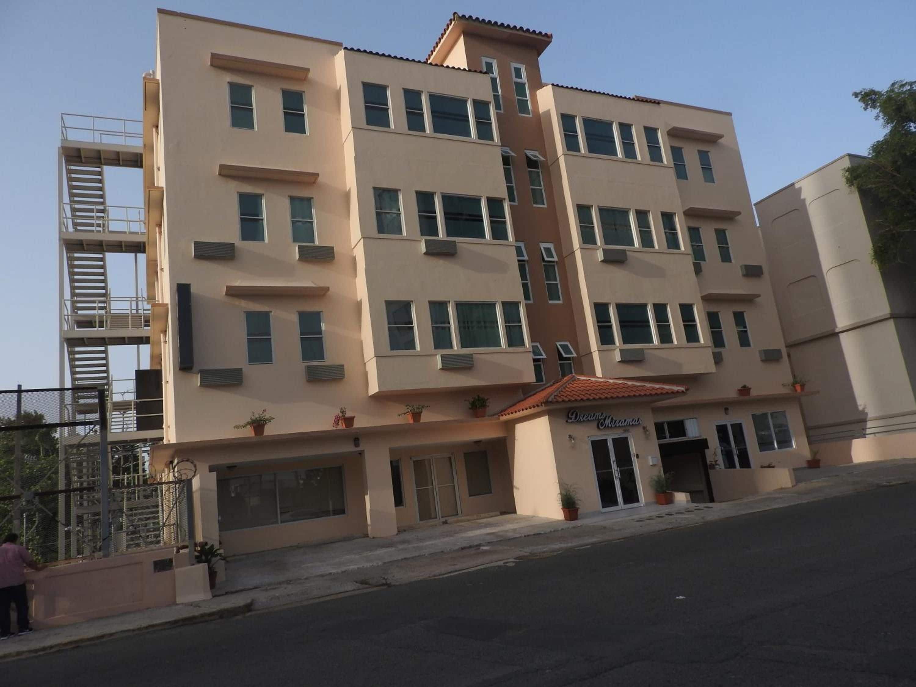 Un hotel de varios pisos con una entrada central, balcones y una escalera contra incendios.