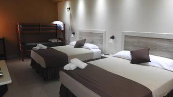 A hotel room with two beds, a bunk bed, a bedside table, and a wall-mounted lamp.