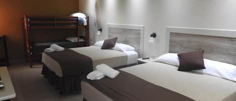 A hotel room with two beds, a bunk bed, a bedside table, and a wall-mounted lamp.