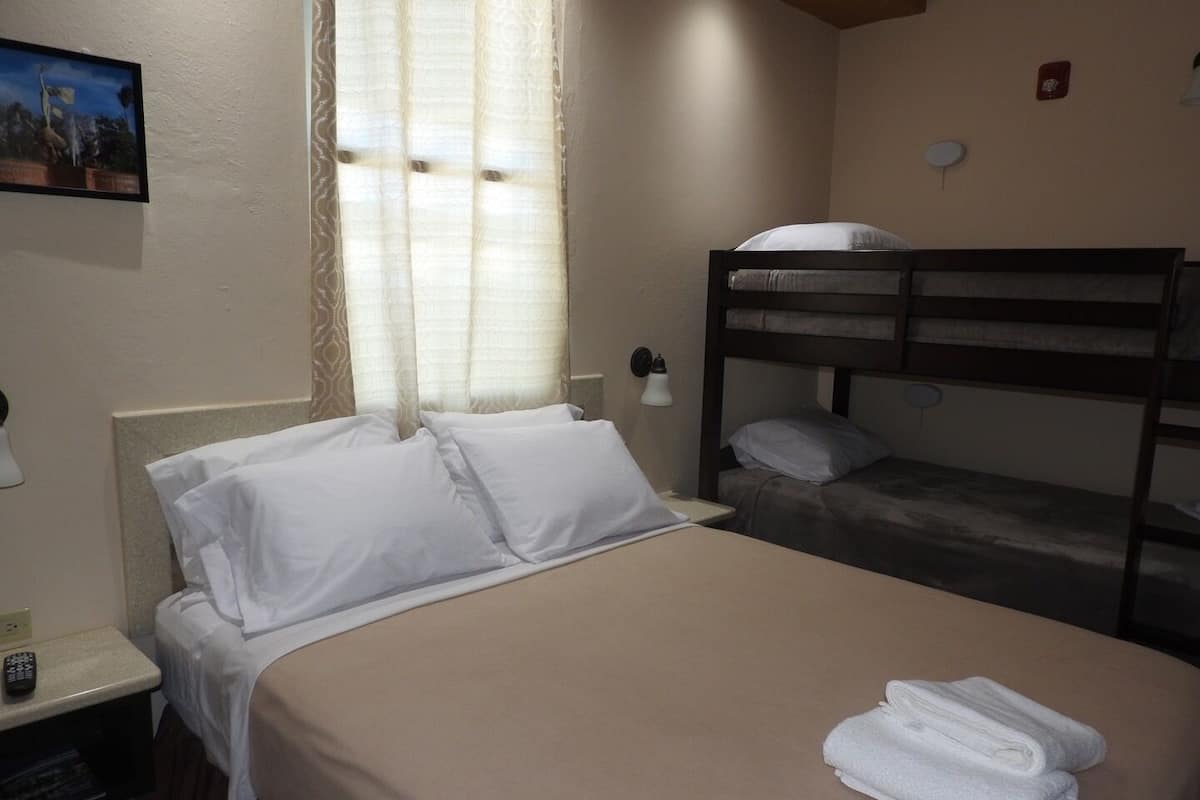 A hotel room with a single bed, a bunk bed, a bedside table with a lamp, and a painting on the wall.