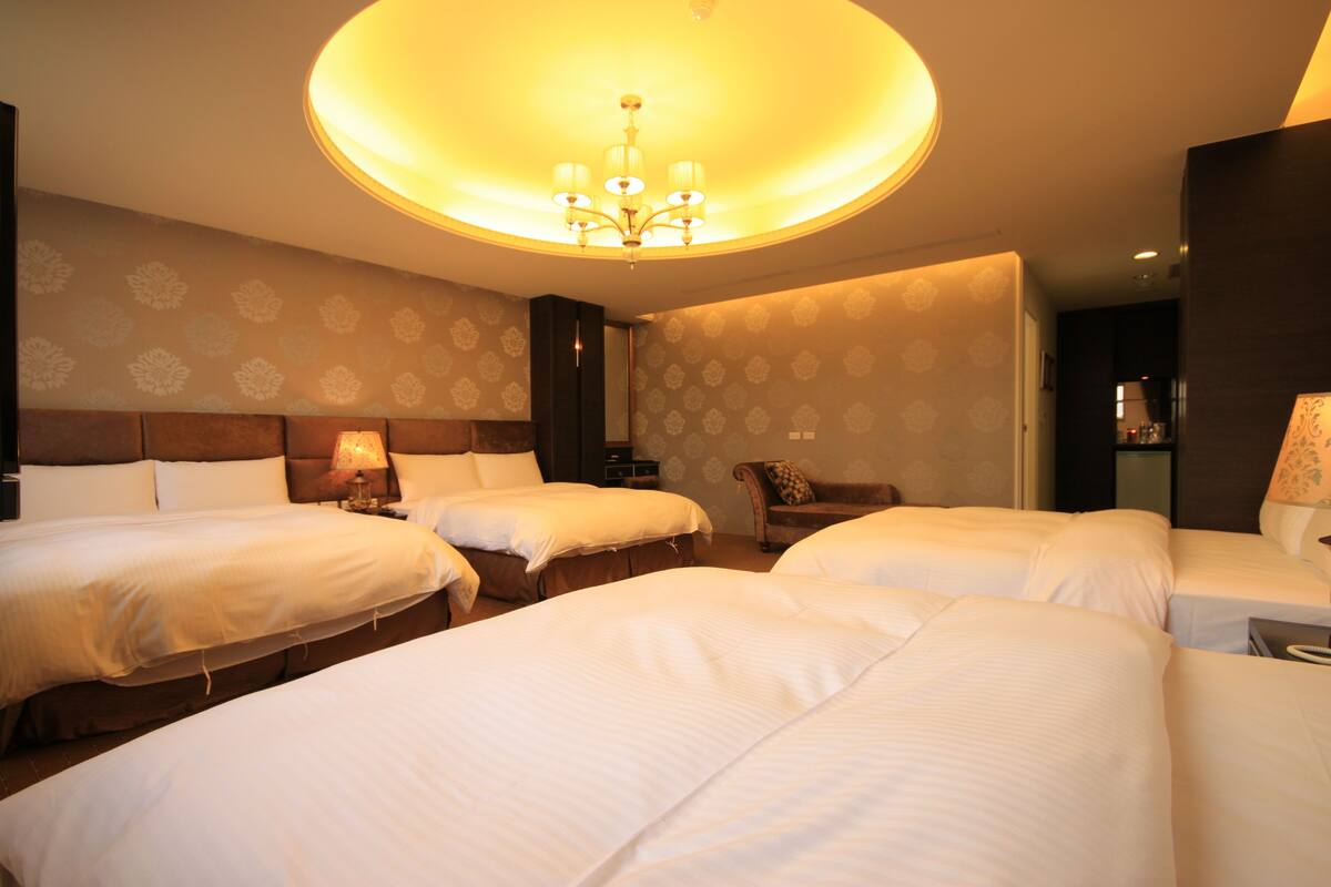 Une chambre d’hôtel avec trois lits, un lustre et un papier peint à motifs.