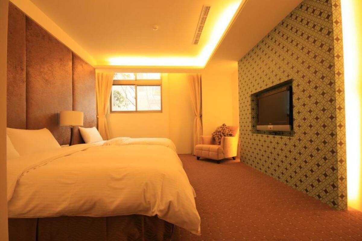 Une chambre d’hôtel avec un grand lit, un téléviseur fixé au mur, une chaise et un papier peint à motifs.
