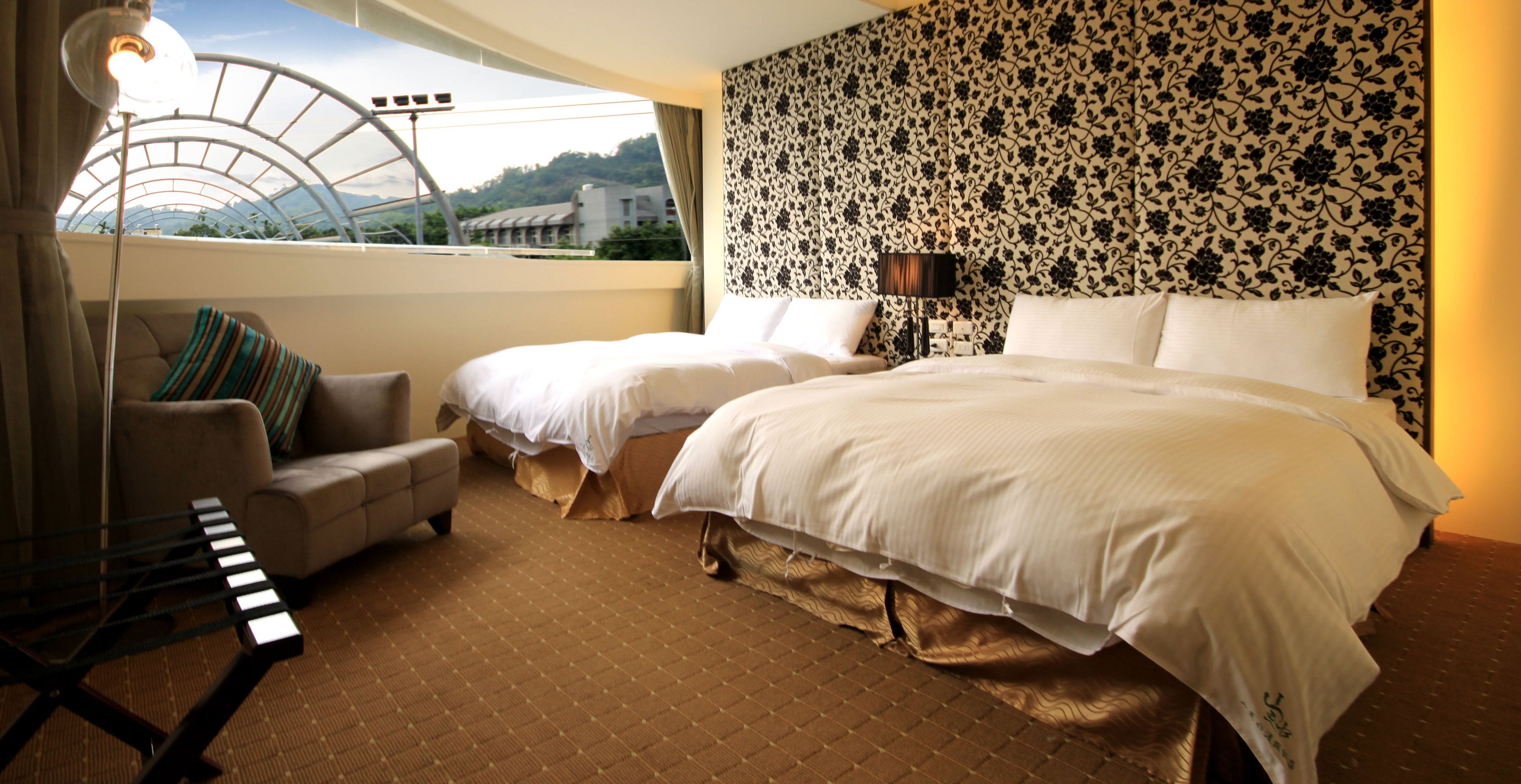 A hotel room with a large bed, a smaller bed, a sofa, and a view of the outdoors.