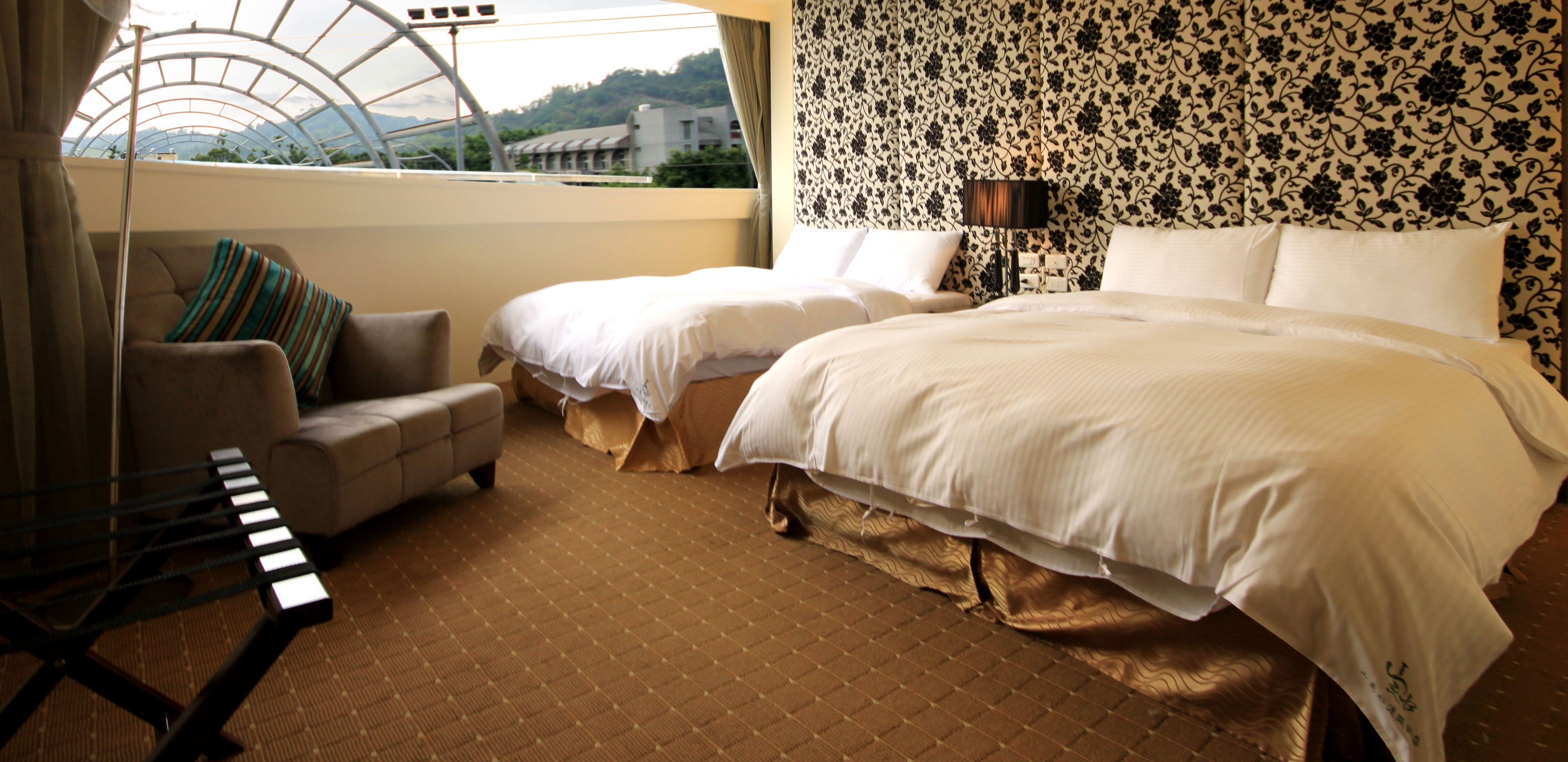 A hotel room with two beds, a sofa, a piano, and a view of a building through a skylight.
