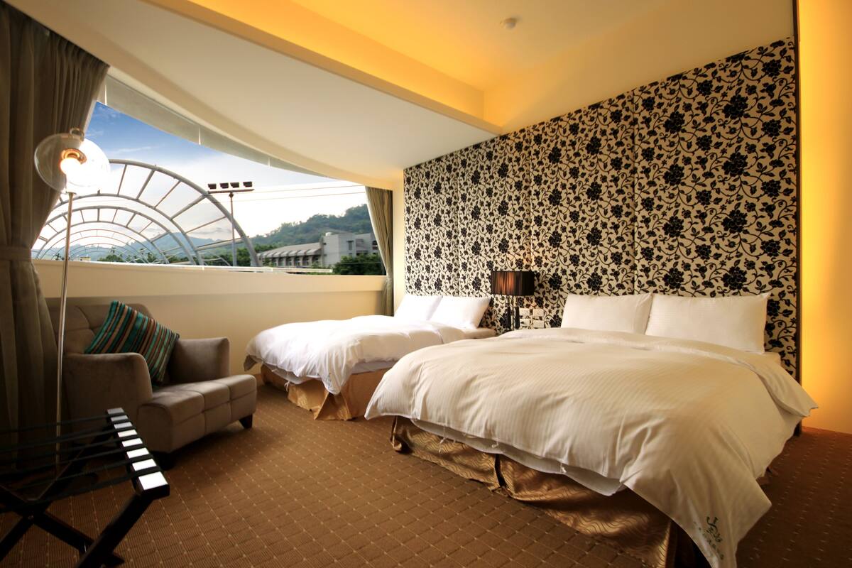 Une chambre d’hôtel avec deux lits, un canapé, un piano et une grande fenêtre donnant sur des immeubles.