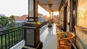 Un balcón con barandilla, una silla de madera y vistas a edificios a lo lejos.