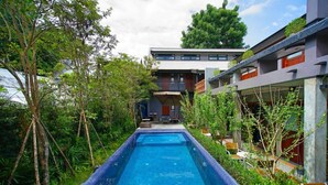 A swimming pool with a view of a modern building and surrounding greenery. - Yellow Pillow Village (Chiang Mai)