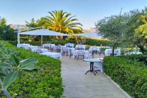 Un área de estar al aire libre con mesas y sillas, rodeada de follaje y palmeras.