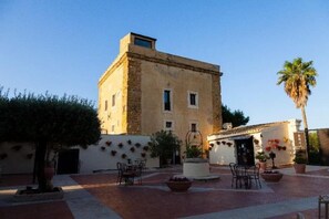 A building with a courtyard, a palm tree, and outdoor seating. - Hotel Foresteria Baglio Della Luna (AGRIGENTO)