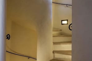 Eine Treppe mit einer Lampe am oberen Ende, einem Türrahmen links und einer Wand mit einem kreisförmigen Muster.