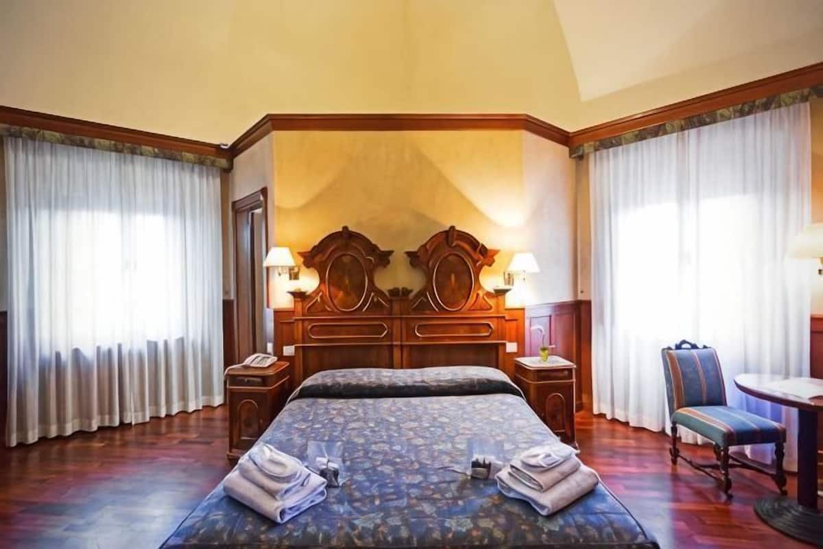 A hotel room with a large bed, two bedside tables with lamps, a chair, and a desk.