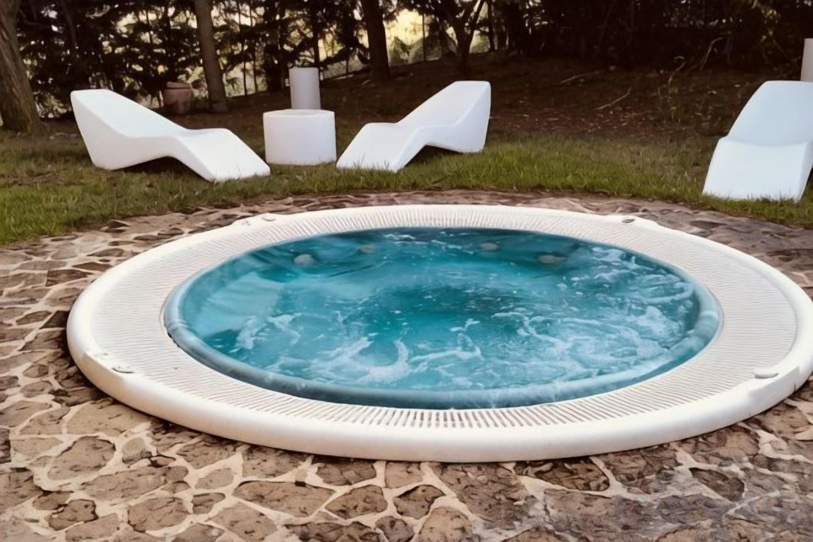 A hot tub surrounded by stone tiles, with white lounge chairs in the background.