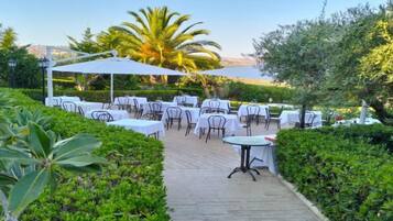 Un área de comedor al aire libre con mesas y sillas, rodeada de vegetación y un cielo despejado.