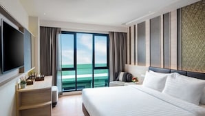A modern hotel room with a large bed, a flat-screen TV, a desk with a chair, and a view of the ocean through large windows. - Chillax Heritage (Bangkok)
