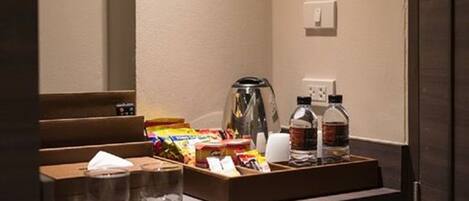 A hotel room with a minibar containing snacks, a coffee maker, and bottled water.