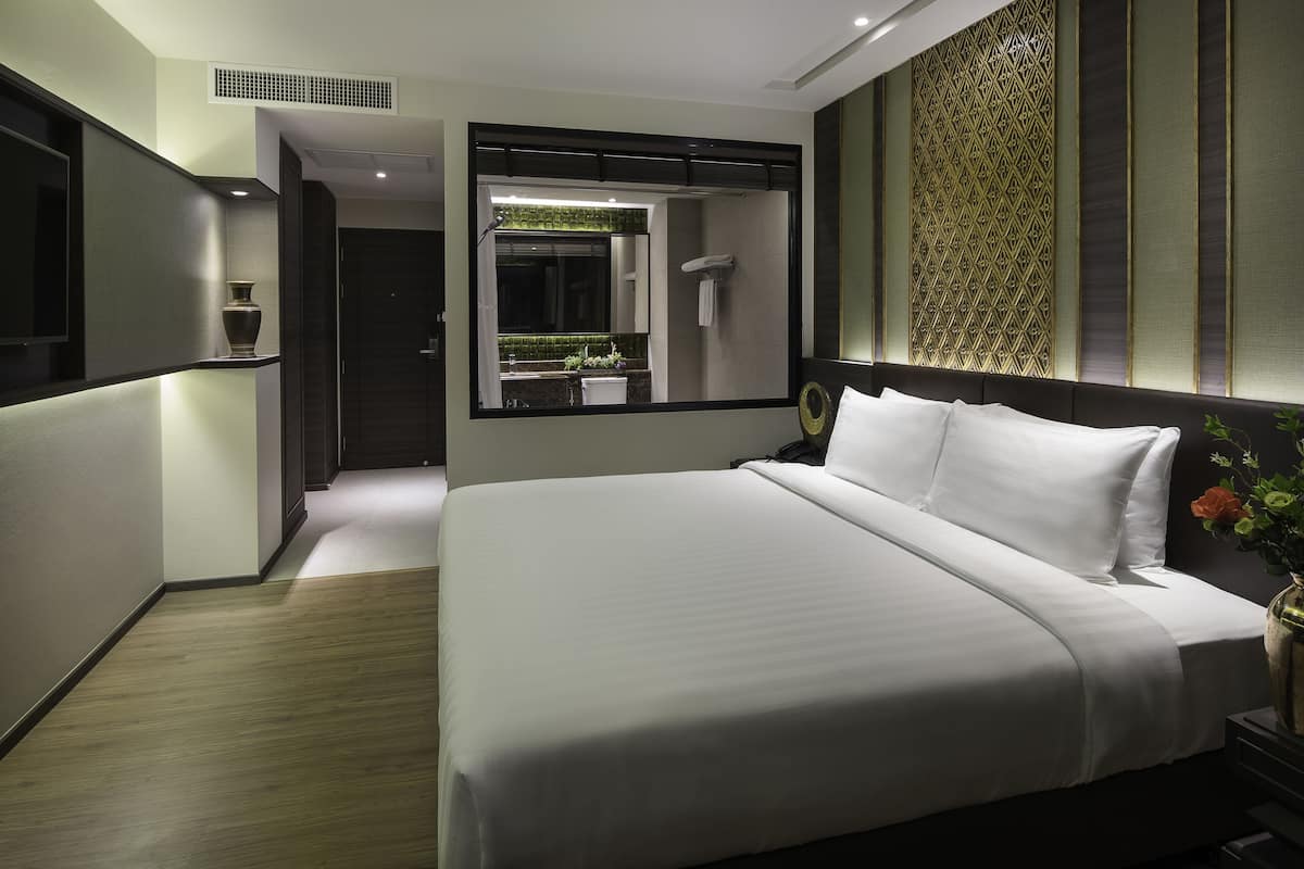 A modern hotel room with a large bed, a mirror, and a shower area.