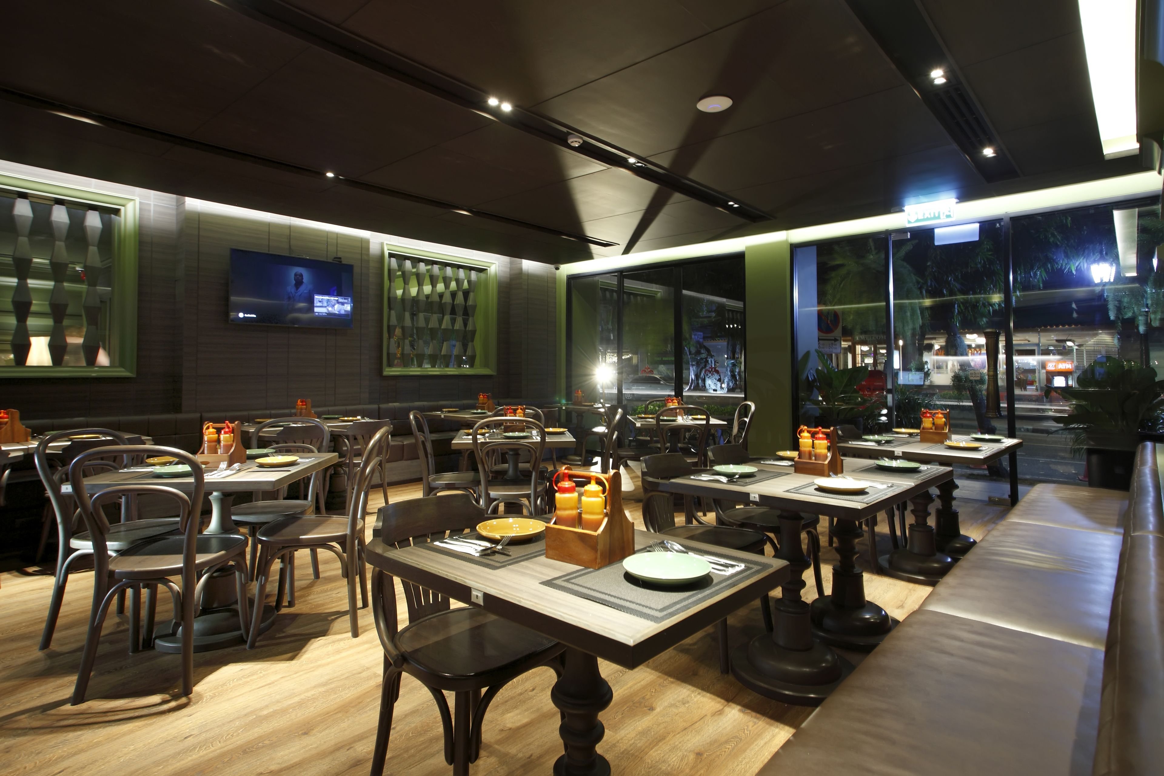 Un restaurant doté de nombreuses tables et chaises, d’un téléviseur fixé au mur et de grandes fenêtres.