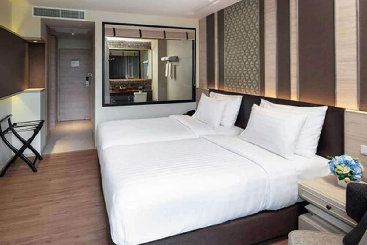 A hotel room with a large bed, a bedside table with a lamp, a mirror, and a view of the bathroom.