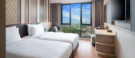 A modern hotel room with two beds, a large window with a city view, a flat-screen TV, and a wooden side table.