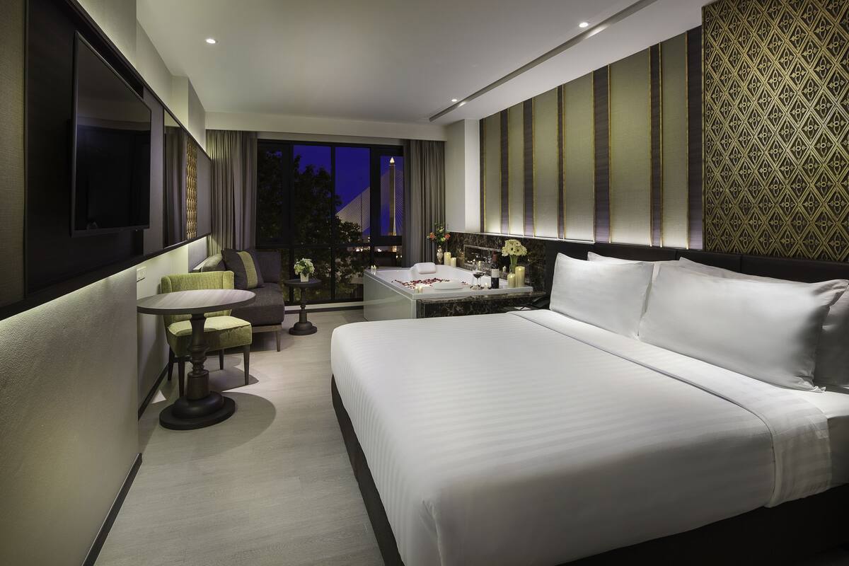 A modern hotel room with a large bed, a small round table, and a seating area with chairs.